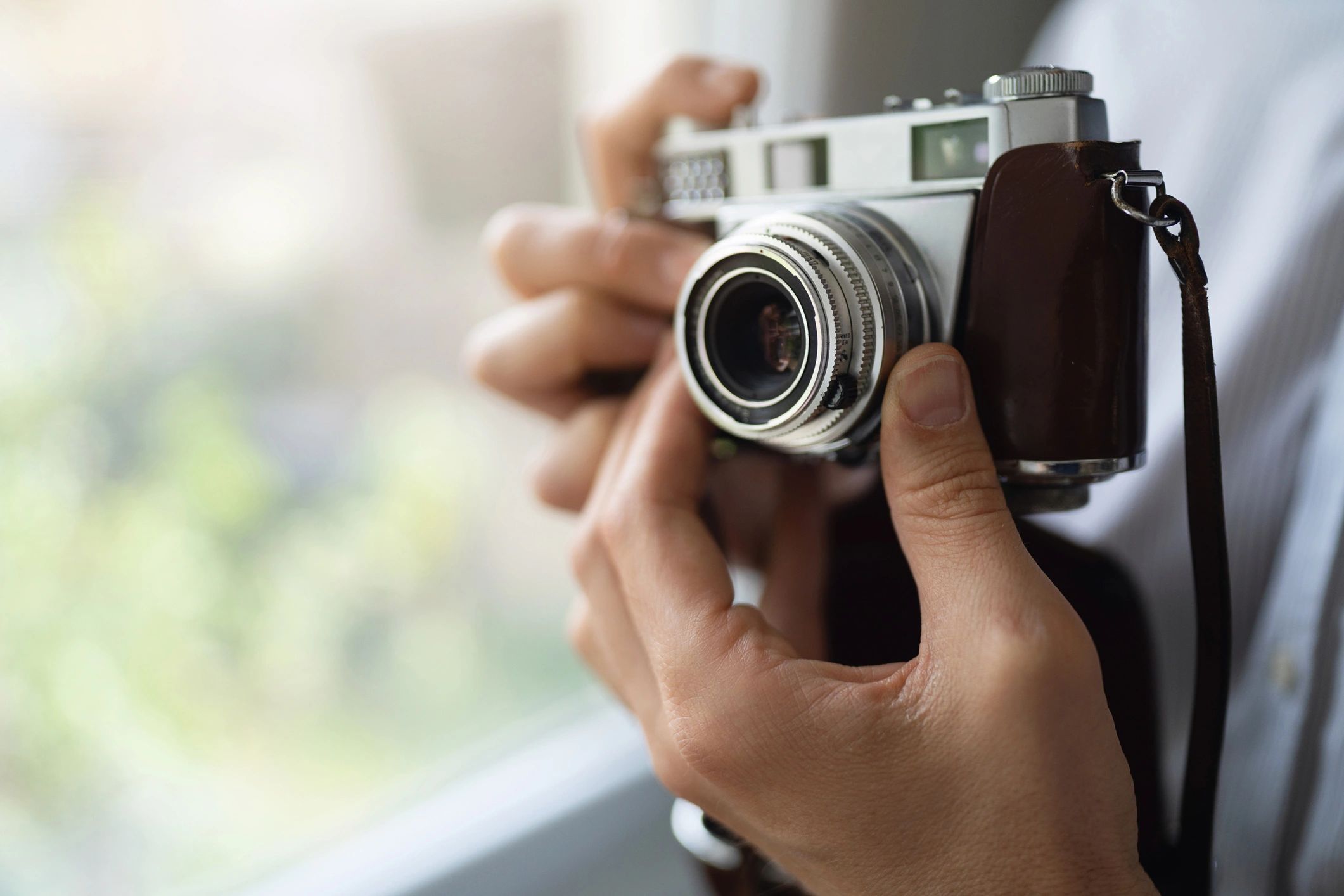 Hands holding a vintage camera near a window
